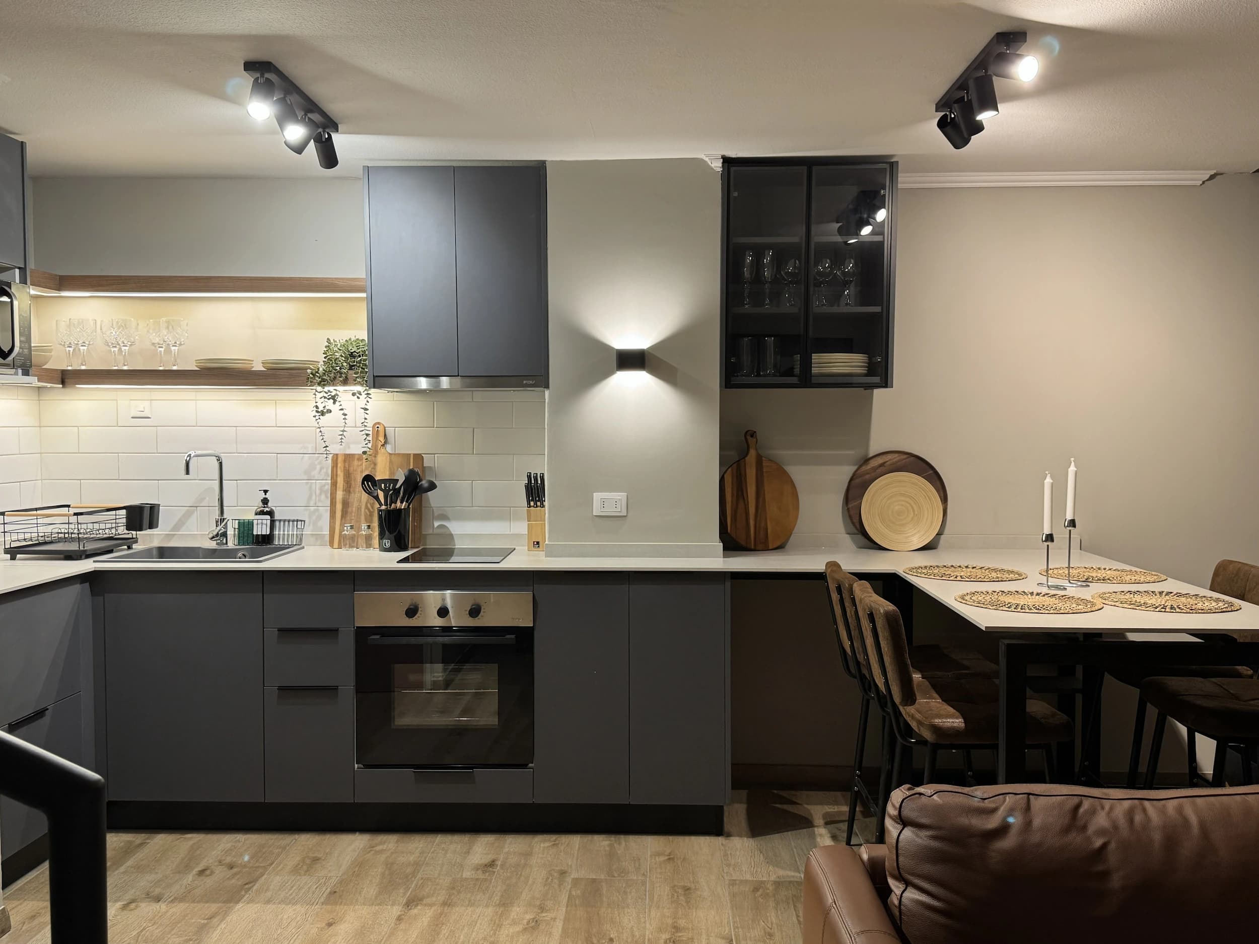 Cocina abierta con muebles gris grafito, encimera clara, cerámica blanca tipo metro y detalles en madera, integrada al comedor.
